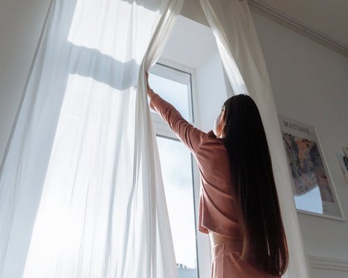 Opening curtains to let morning sunlight in